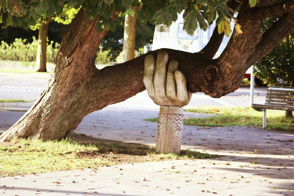 A stone sculpture of a hand emerging from the ground to support a heavy tree branch.