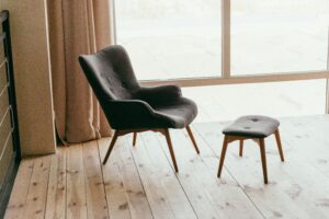 Grey tufted chair with ottoman seated in front of a window on beige wood floor, therapyworthwhile