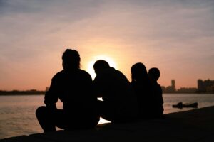 Silhouette of backside of four people, sitting before the beach and sunset, therapyworthwhile