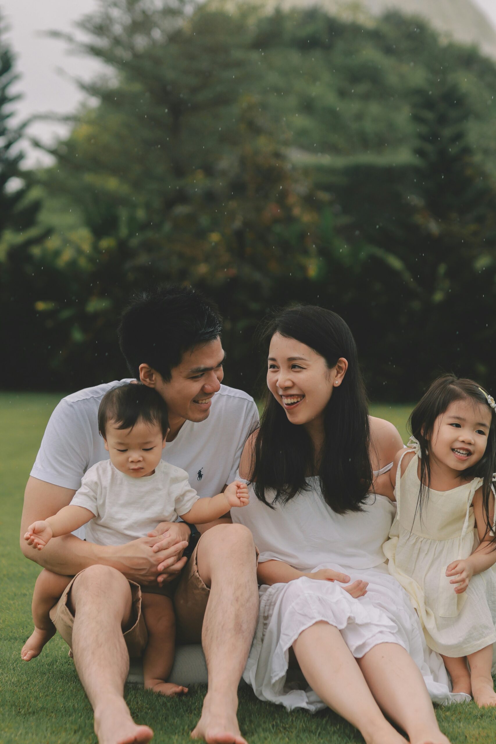 Family of four, sitting in a grass meadow, smiling. A dad, mom, daughter, and son, therapyworthwhile