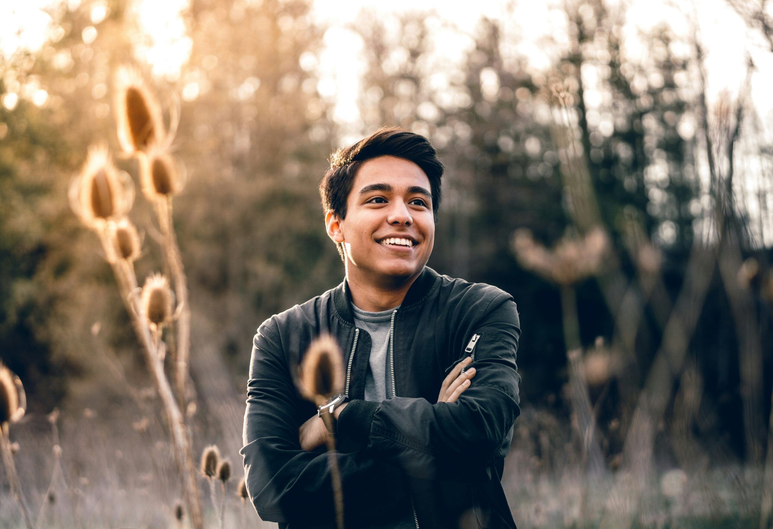 Brunette male standing, smiling, with arms folded in a field of tall grass, therapyworthwhile