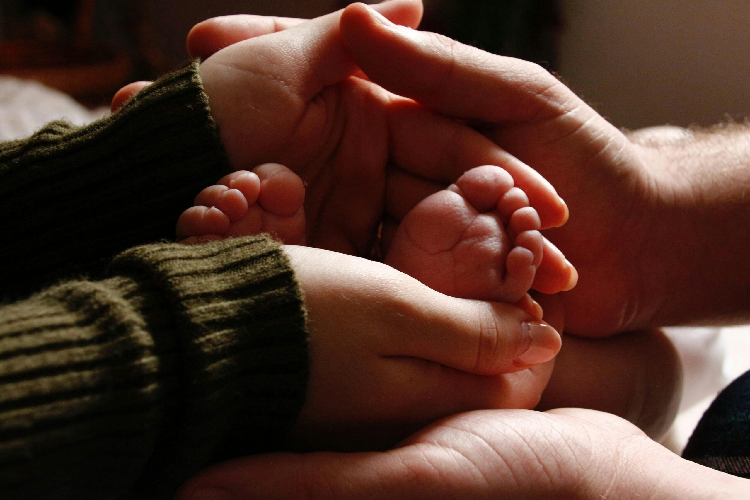 Two adult set of hands holding onto newborn feet, therapyworthwhile