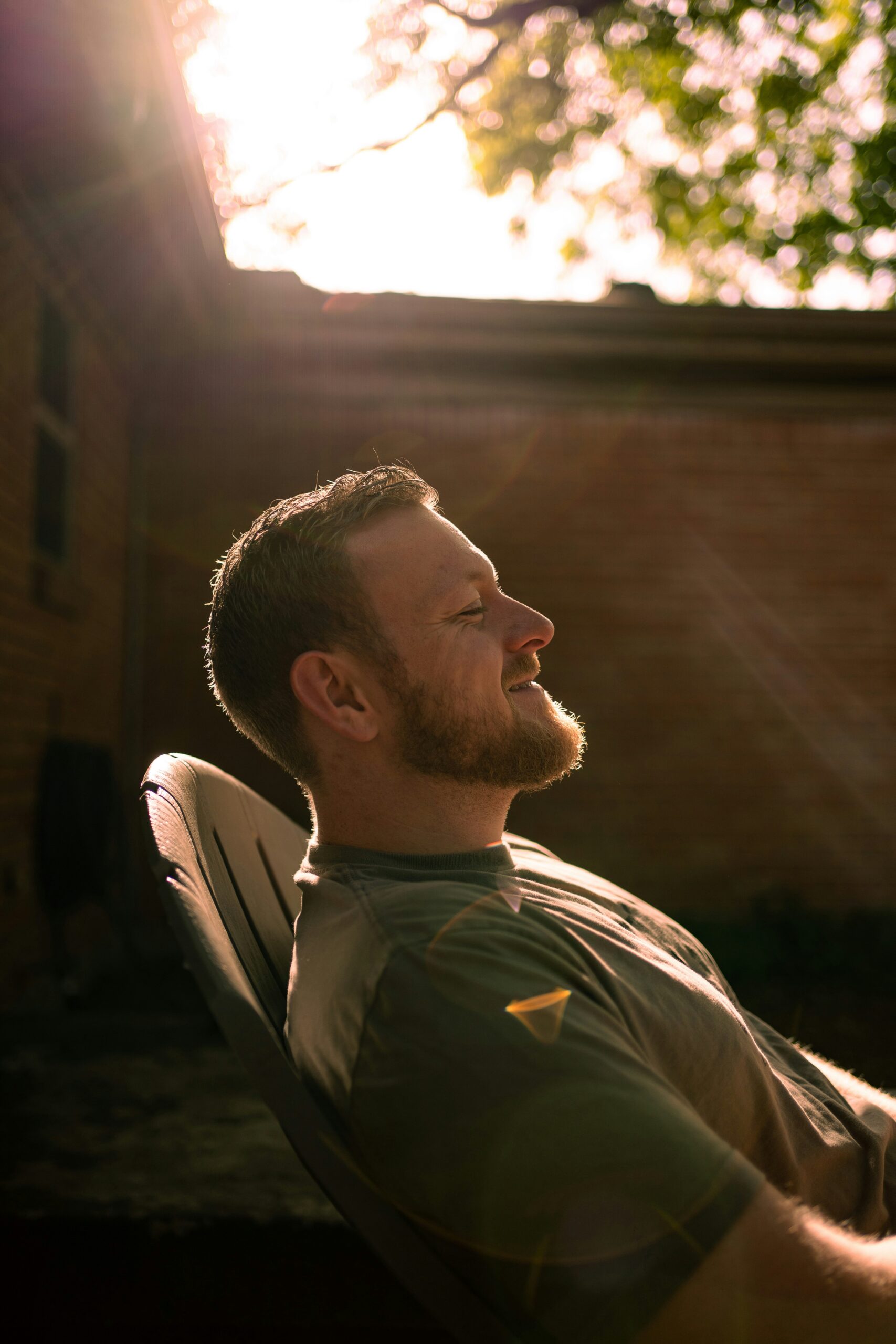 Male sitting outside on a lawn chair, eyes closed, soft grin on face, relaxing