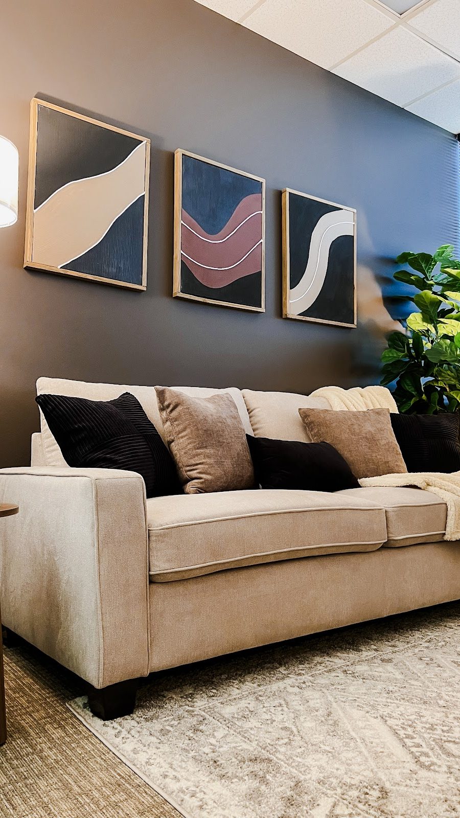 Modern beige sofa in a cozy therapy room with three abstract wall paintings and a floor lamp, therapyworthwhile